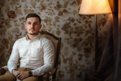 رجل شاب أنيق يجلس في غرفة معيشة دافئة مع إضاءة ناعمة